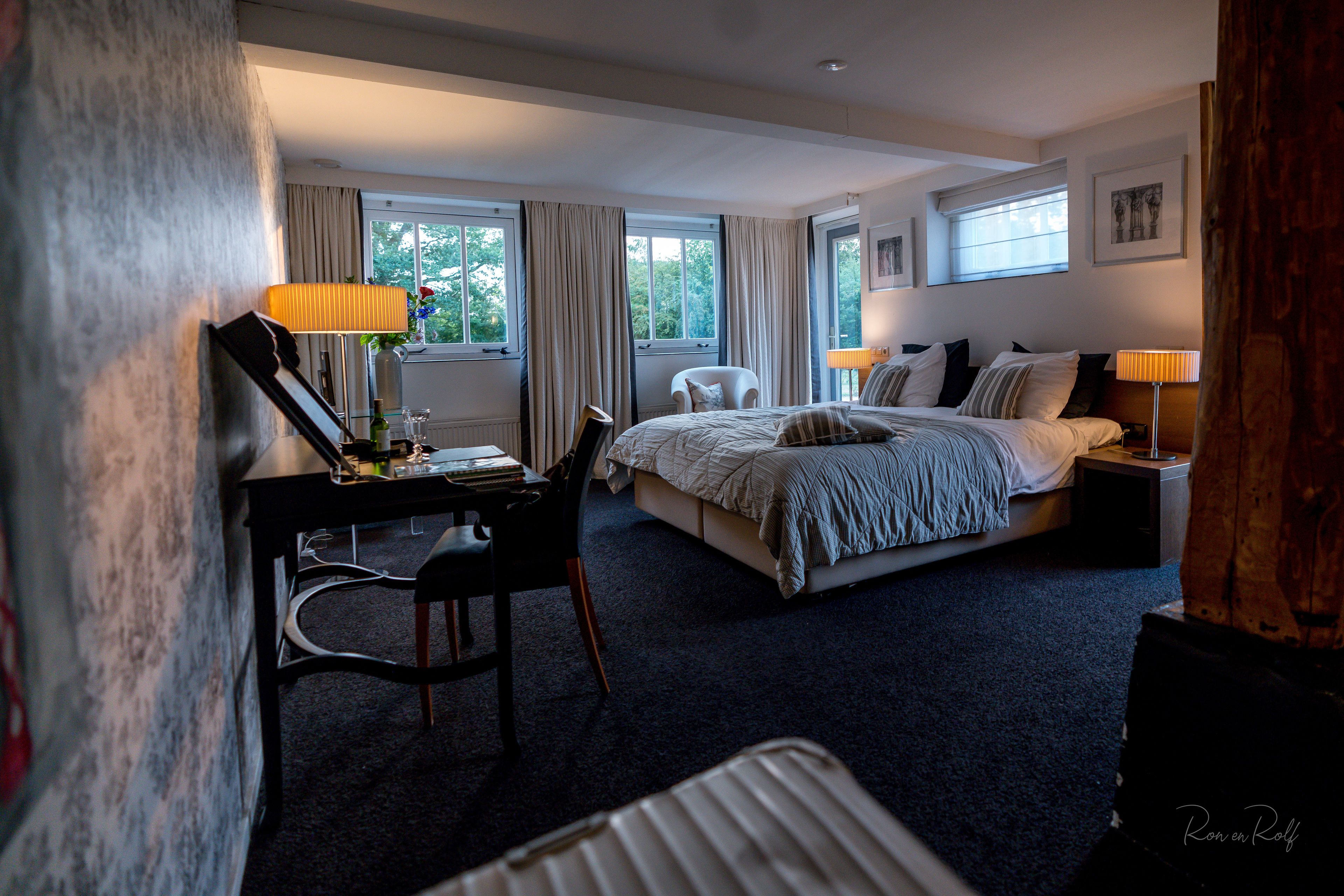 A hotel room with a bed, desk, chair, and two bedside lamps.