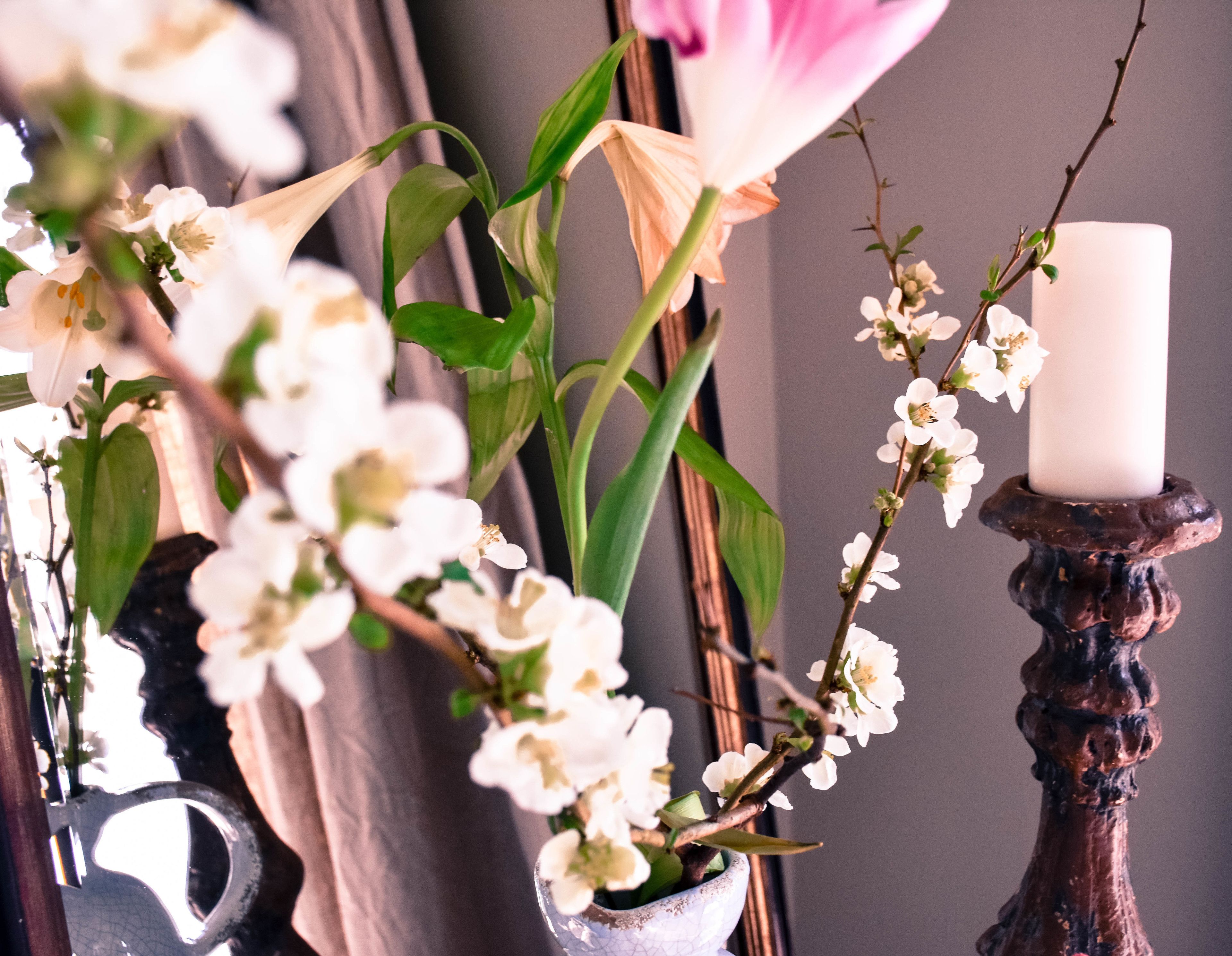 Een kaars op een houten standaard, omringd door witte bloemen en groene bladeren.