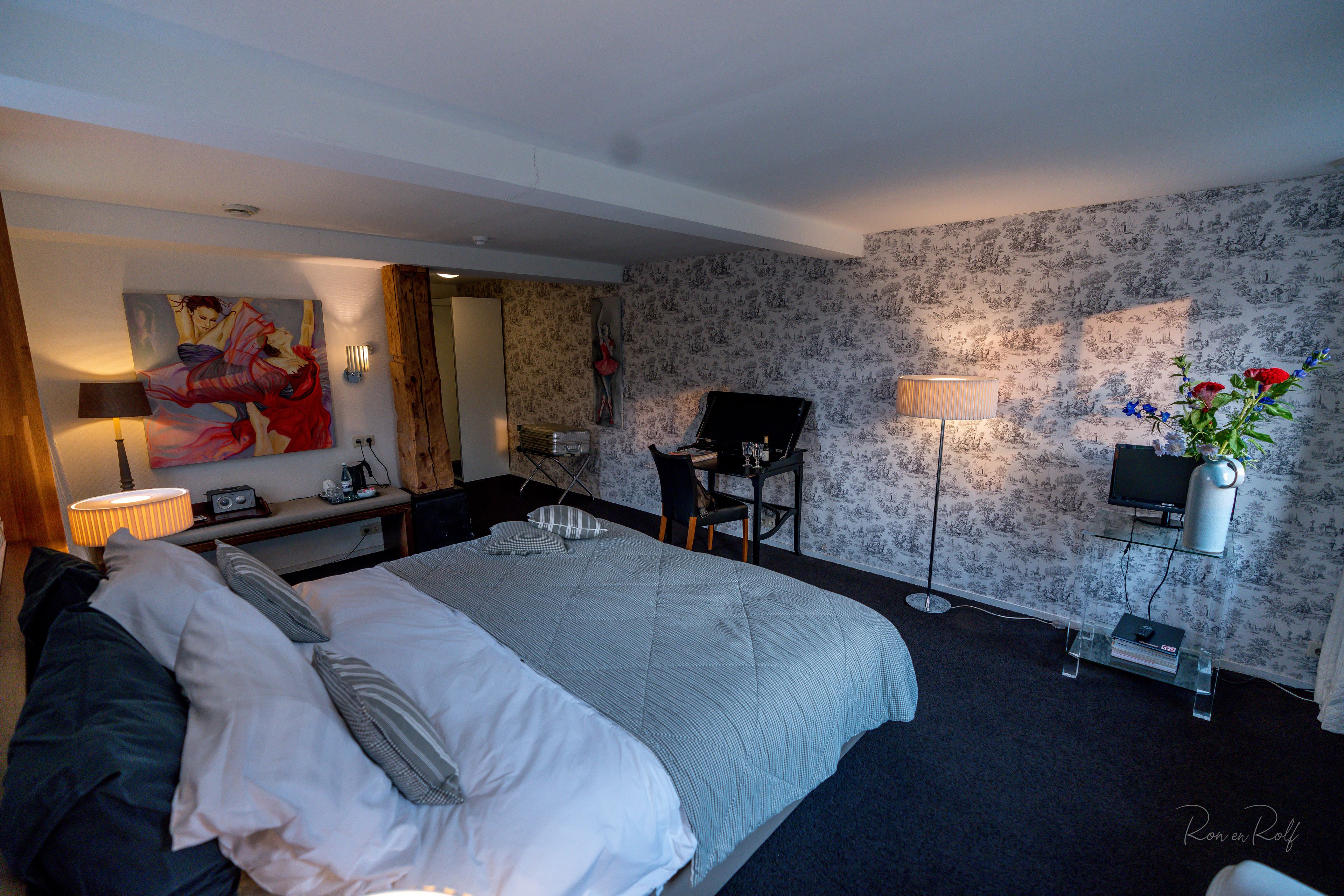 A hotel room with a large bed, a desk with a chair, a TV, and a plant.