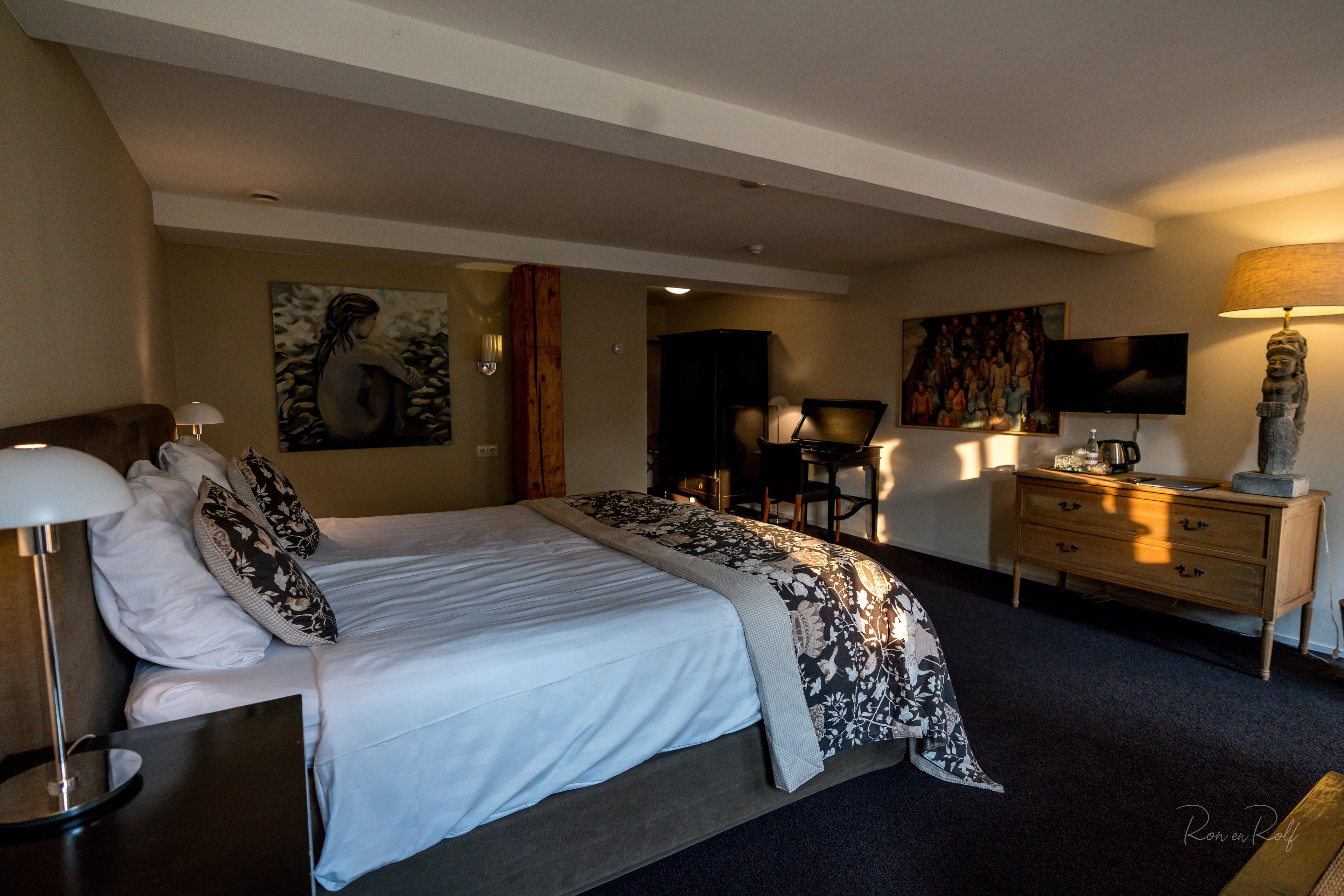 A hotel room with a large bed, a desk, a chair, a dresser, a television, and artwork on the walls.