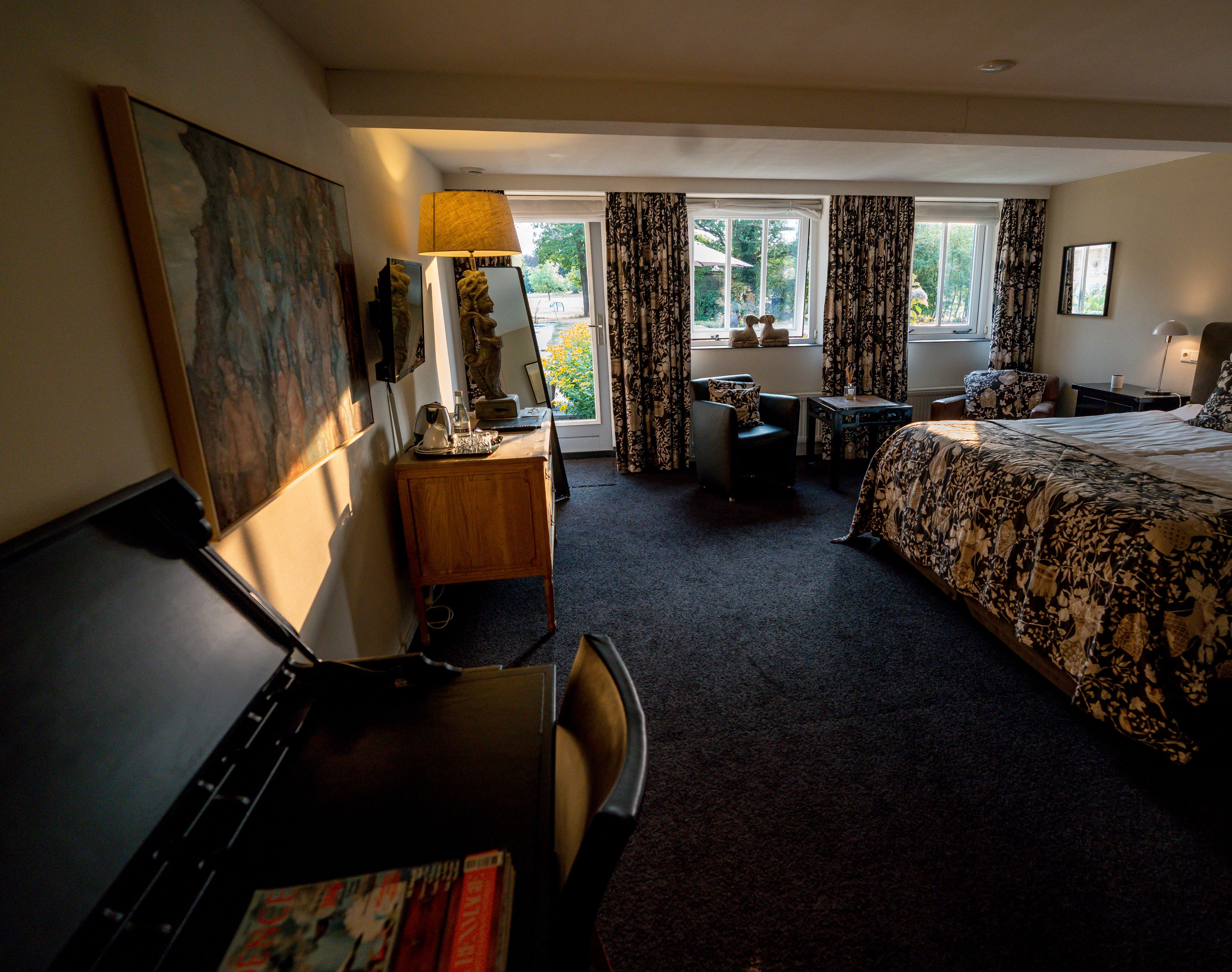 Ein Hotelzimmer mit Bett, Schreibtisch, Stuhl und einem großen Fenster mit Vorhängen.