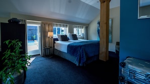 Een slaapkamer met een bed, nachtkastje, lamp, een potplant en een koffer.
