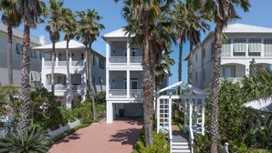 A multi-story white building with balconies, surrounded by palm trees and a white picket fence. - Paradise Found - Private Beachfront House 3 Bedroom Home by RedAwning (South Padre Island)