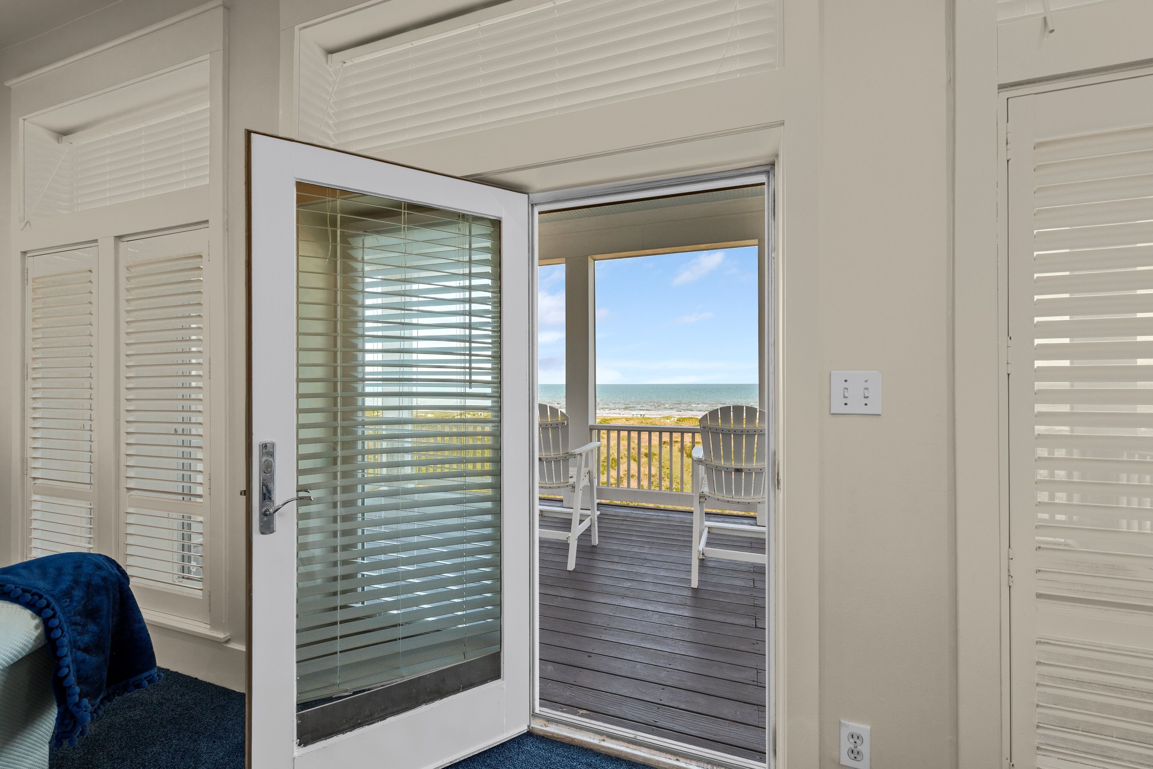 A room with a sliding glass door leading to a balcony with a view of the beach.