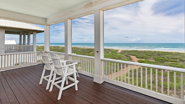 A covered outdoor area with a view of the ocean, featuring a wooden deck, white railings, and a table with chairs. - Paradise Found - Private Beachfront House 3 Bedroom Home by RedAwning (South Padre Island)