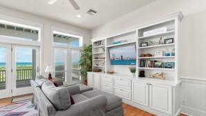 A spacious living room with a gray sectional sofa, a large flat-screen TV, and a white built-in shelving unit with various decorative items. - Paradise Found - Private Beachfront House 3 Bedroom Home by RedAwning (South Padre Island)