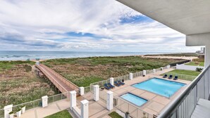Une piscine sur le toit, dotée de chaises longues, offrant une vue sur la plage et entourée d’une structure en béton.