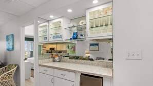 A modern kitchen with white cabinets, a granite countertop, and glass shelving above. - Edgewater Unit #303 2 Bedroom Apts by RedAwning (South Padre Island)