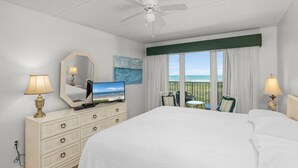 A hotel room with a bed, a television, a dresser, a mirror, a window with a view, and a ceiling fan. - Edgewater Unit #303 2 Bedroom Apts by RedAwning (South Padre Island)