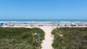 A beach with a sandy path leading to the ocean, surrounded by greenery. - Edgewater Unit #303 2 Bedroom Apts by RedAwning (South Padre Island)