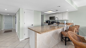 A modern kitchen with a central island, white cabinets, and a breakfast bar with wicker chairs. - Beach House Unit #302 2 Bedroom Condo by RedAwning (South Padre Island)