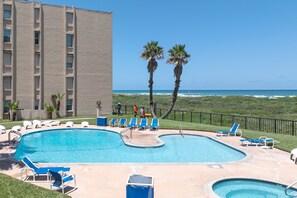 A swimming pool with blue chairs and palm trees, surrounded by a fence and a building. - Beach House Unit #302 2 Bedroom Condo by RedAwning (South Padre Island)