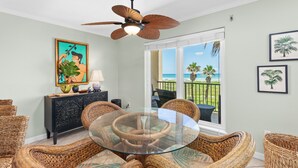 A dining area with wicker furniture, a glass table, and a ceiling fan. - Beach House Unit #302 2 Bedroom Condo by RedAwning (South Padre Island)