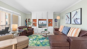 A living room with a sofa, armchair, coffee table, and a view of the kitchen through an open door. - Beach House Unit #302 2 Bedroom Condo by RedAwning (South Padre Island)