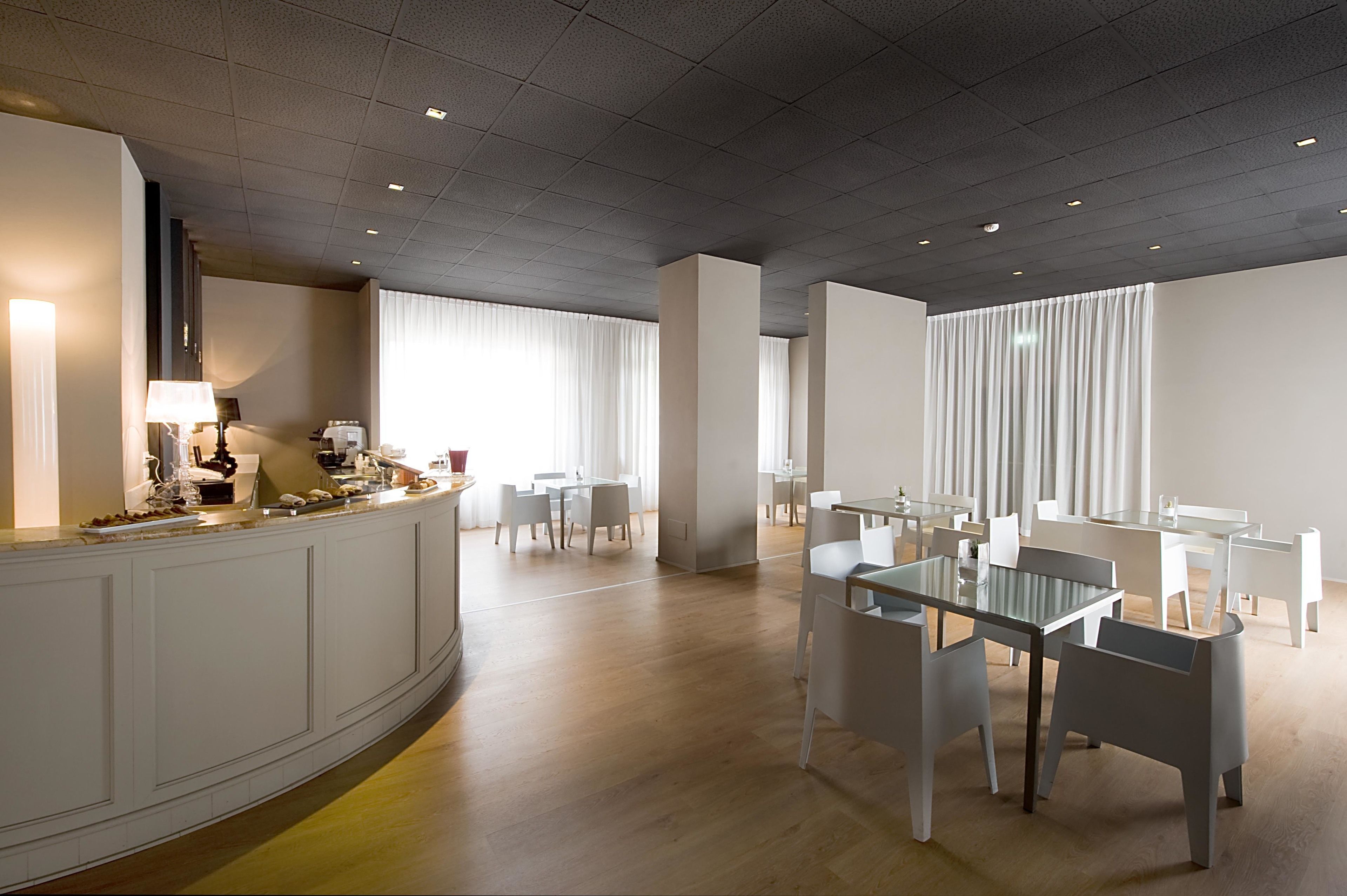 A modern dining area with white furniture, a curved counter, and large windows with sheer curtains.
