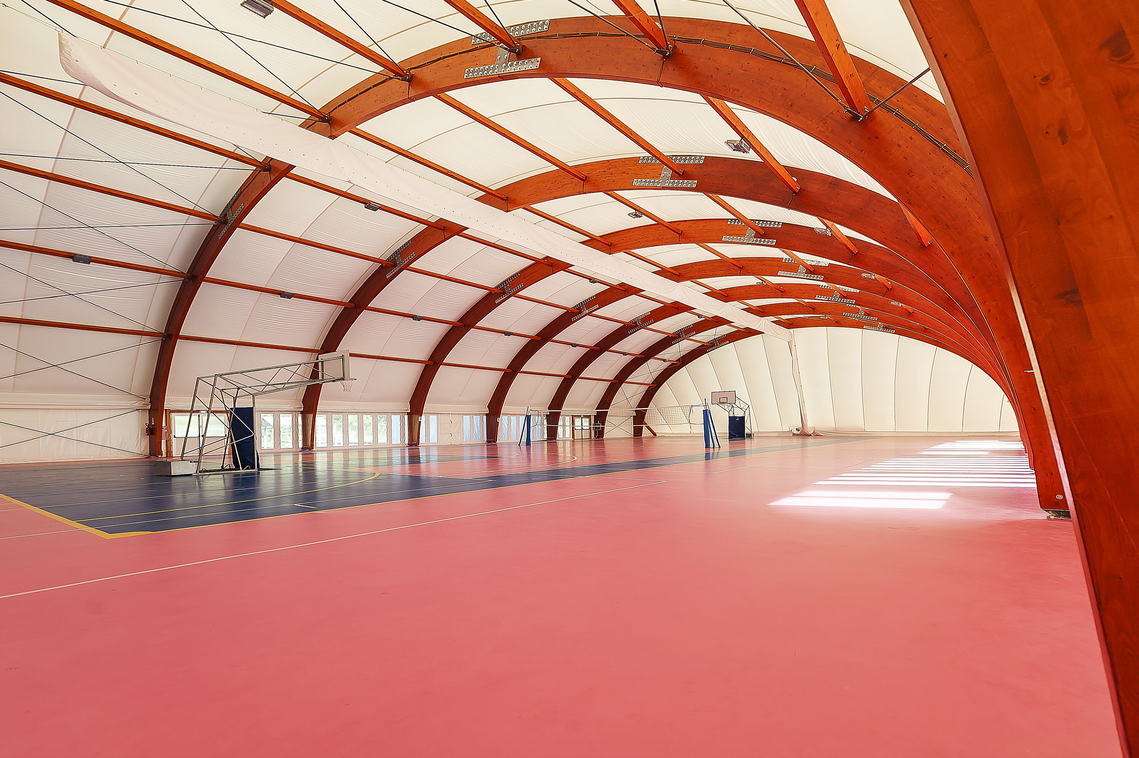 An indoor sports facility with a high ceiling, a basketball court, and a climbing wall.
