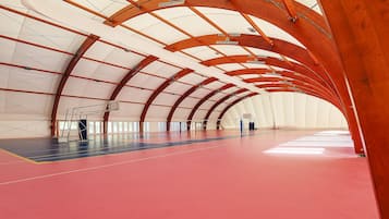 An indoor sports facility with a high ceiling, a basketball court, and a climbing wall.