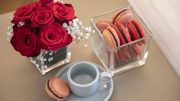 A table with a vase of red roses, a clear glass container with macarons, and a blue cup and saucer.