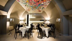 A dining area with tables set for a meal, a ceiling with a colorful abstract design, and modern lighting fixtures. - Hotel La Corte (Cascia)