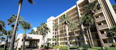 A multi-story hotel with a central courtyard, palm trees, and a clear blue sky.