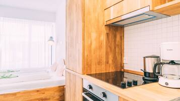 A modern kitchen with wooden cabinets, a stove, a coffee maker, and a window with sheer curtains.