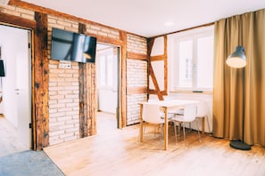 Una habitación moderna con paredes de ladrillo visto, un televisor de pantalla plana montado en la pared, una mesa de comedor con sillas y un ventanal con cortinas.