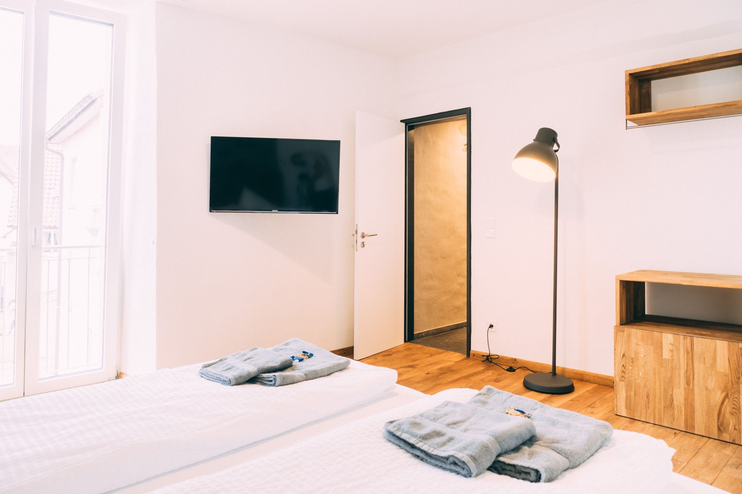A hotel room with a bed, a television, a desk, and a floor lamp.