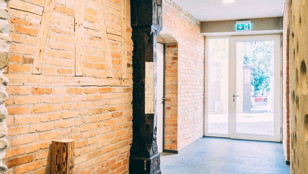 Un pasillo con paredes de ladrillo, un poste de madera y una puerta que da al exterior.