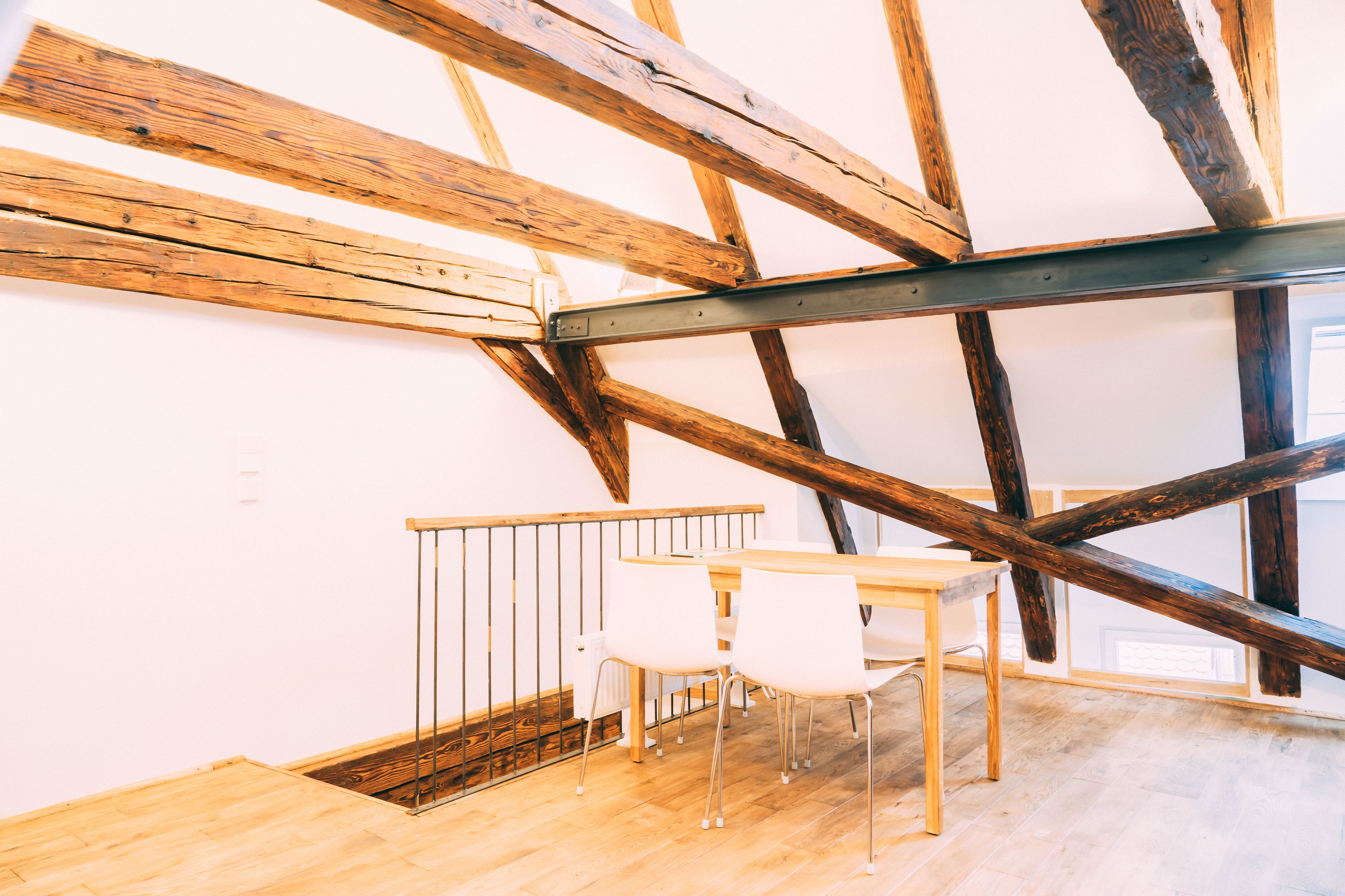A room with exposed wooden beams, a wooden table with chairs, and a window providing natural light.