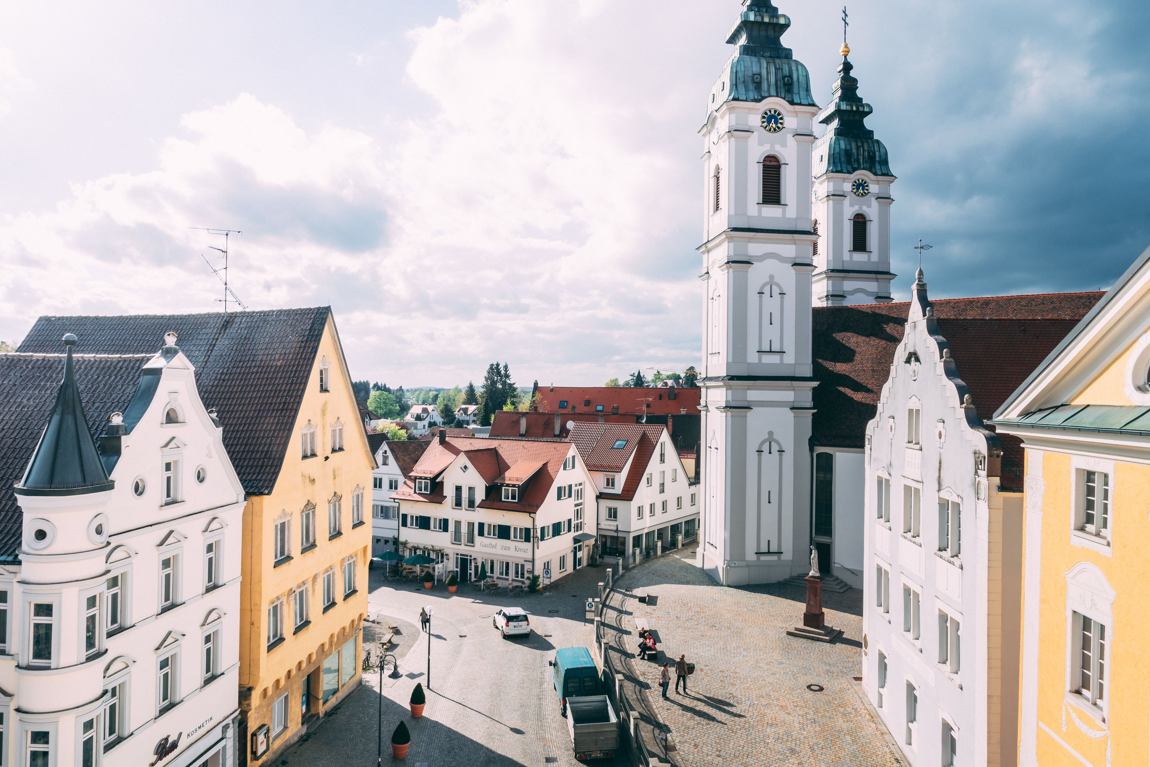 A historic town square with traditional architecture, including a prominent clock tower and a church.