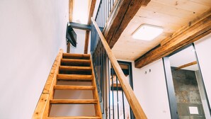 Una escalera de madera con barandilla metálica que lleva a un cuarto con pared de azulejos y una puerta.