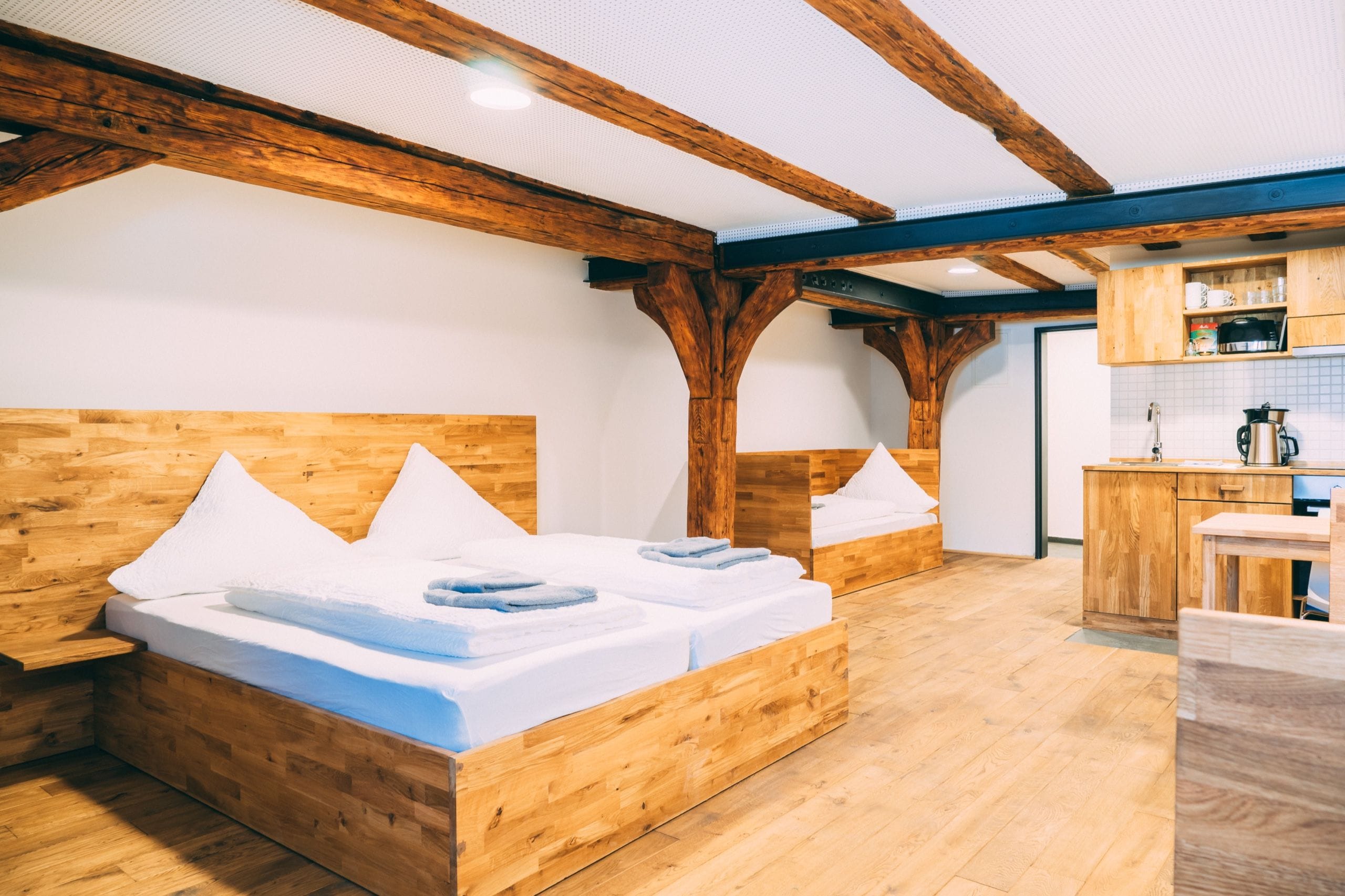 Une chambre avec deux lits en bois, un coin cuisine et des poutres en bois au plafond.