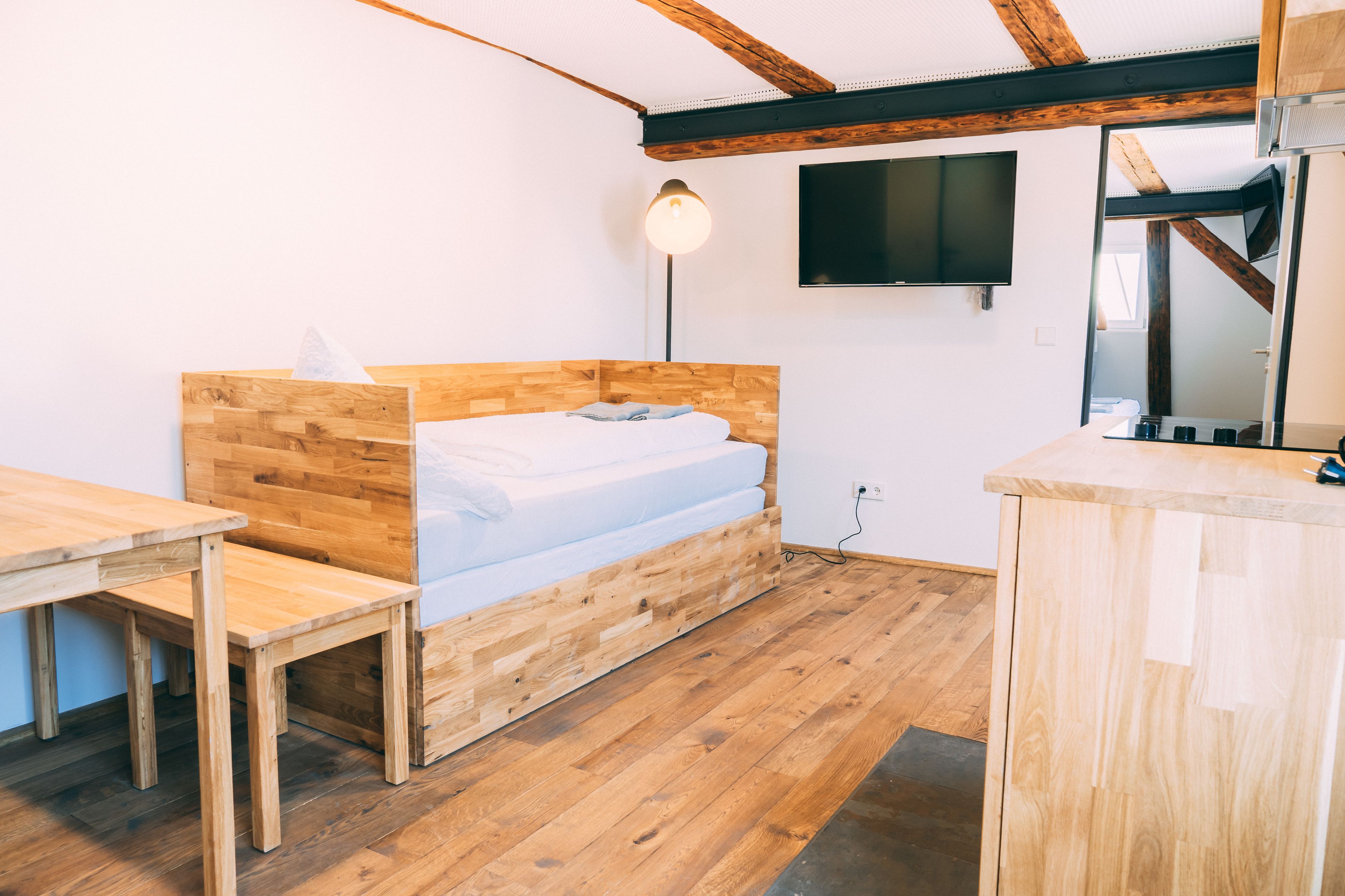 Una habitación pequeña con estructura de madera, que incluye una cama, un escritorio y un televisor montado en la pared.
