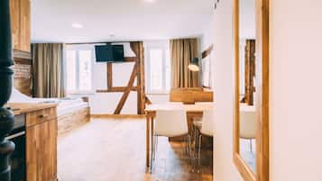 A modern interior with a wooden dining table, chairs, a TV mounted on a wall, and a staircase leading to an upper level.