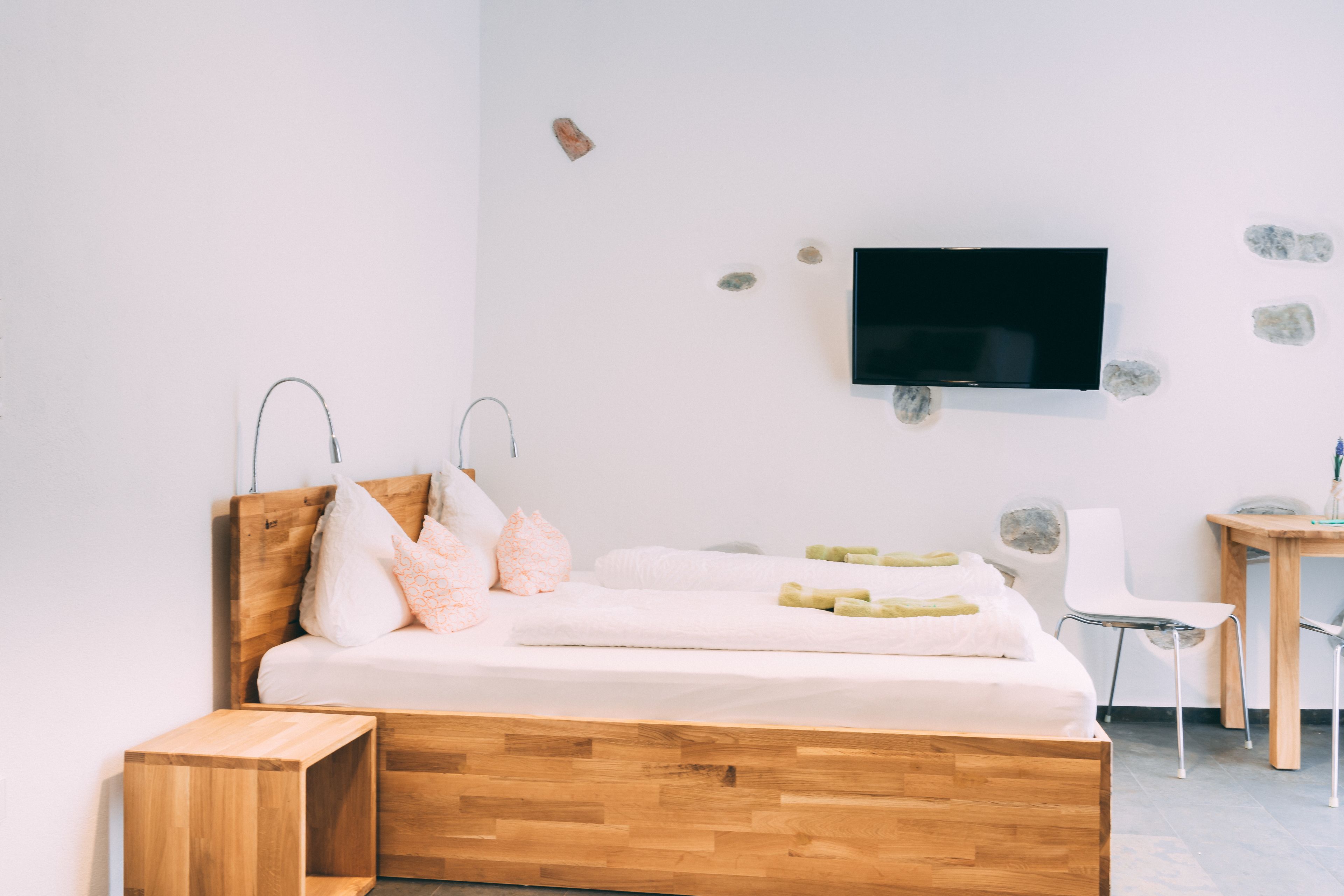 Une chambre à coucher moderne avec un lit en bois, un téléviseur fixé au mur, un petit bureau et une chaise.
