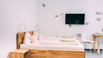 Une chambre à coucher moderne avec un lit en bois, un téléviseur fixé au mur, un petit bureau et une chaise.