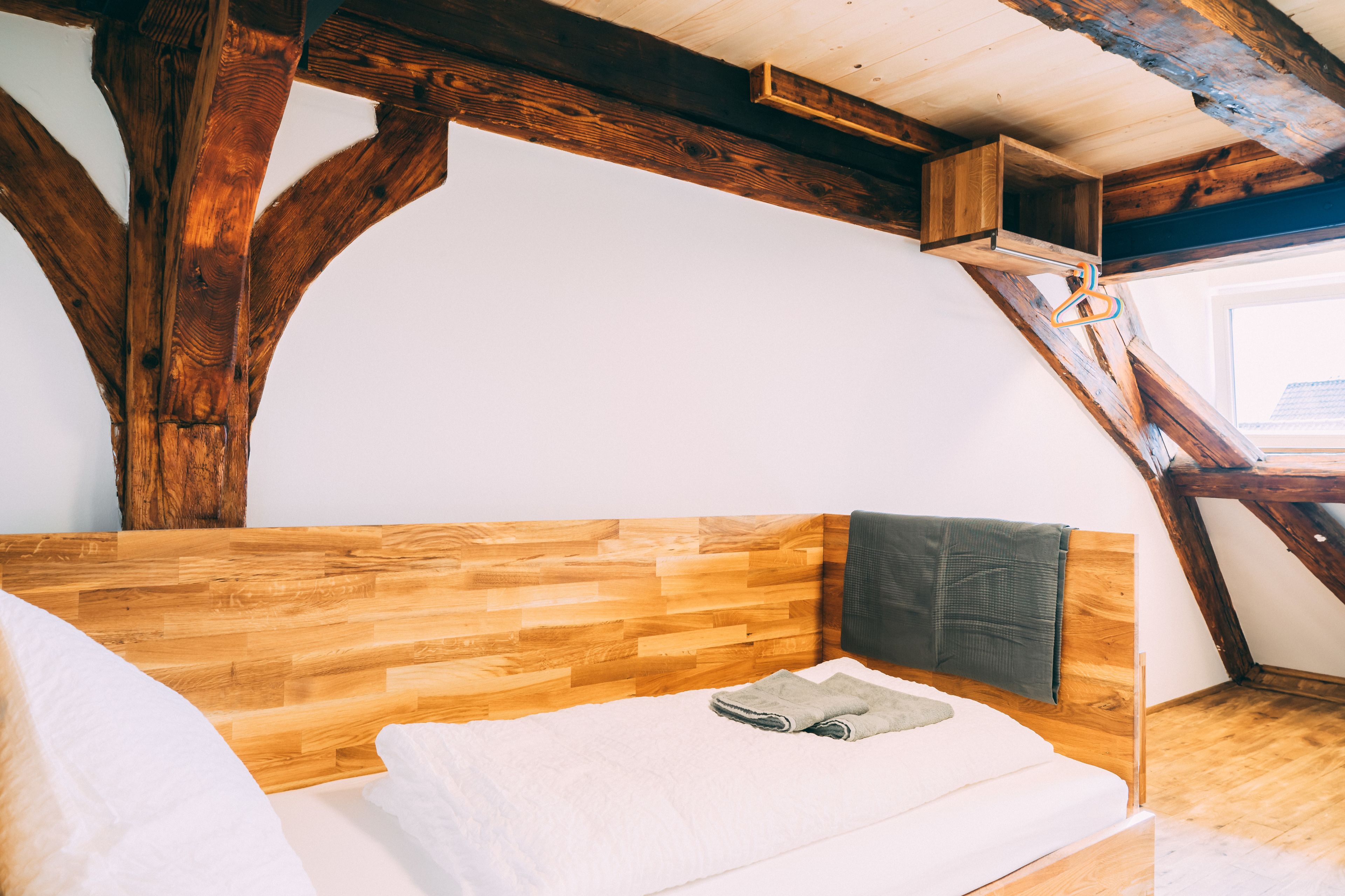 A cozy loft bedroom with exposed wooden beams, a wooden headboard, and a small window.