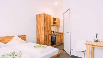 A bedroom with a wooden bed, a small kitchenette, and a white chair.