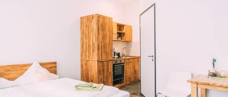 Un dormitorio con una cama de madera, un pequeño kitchenette y una silla blanca.