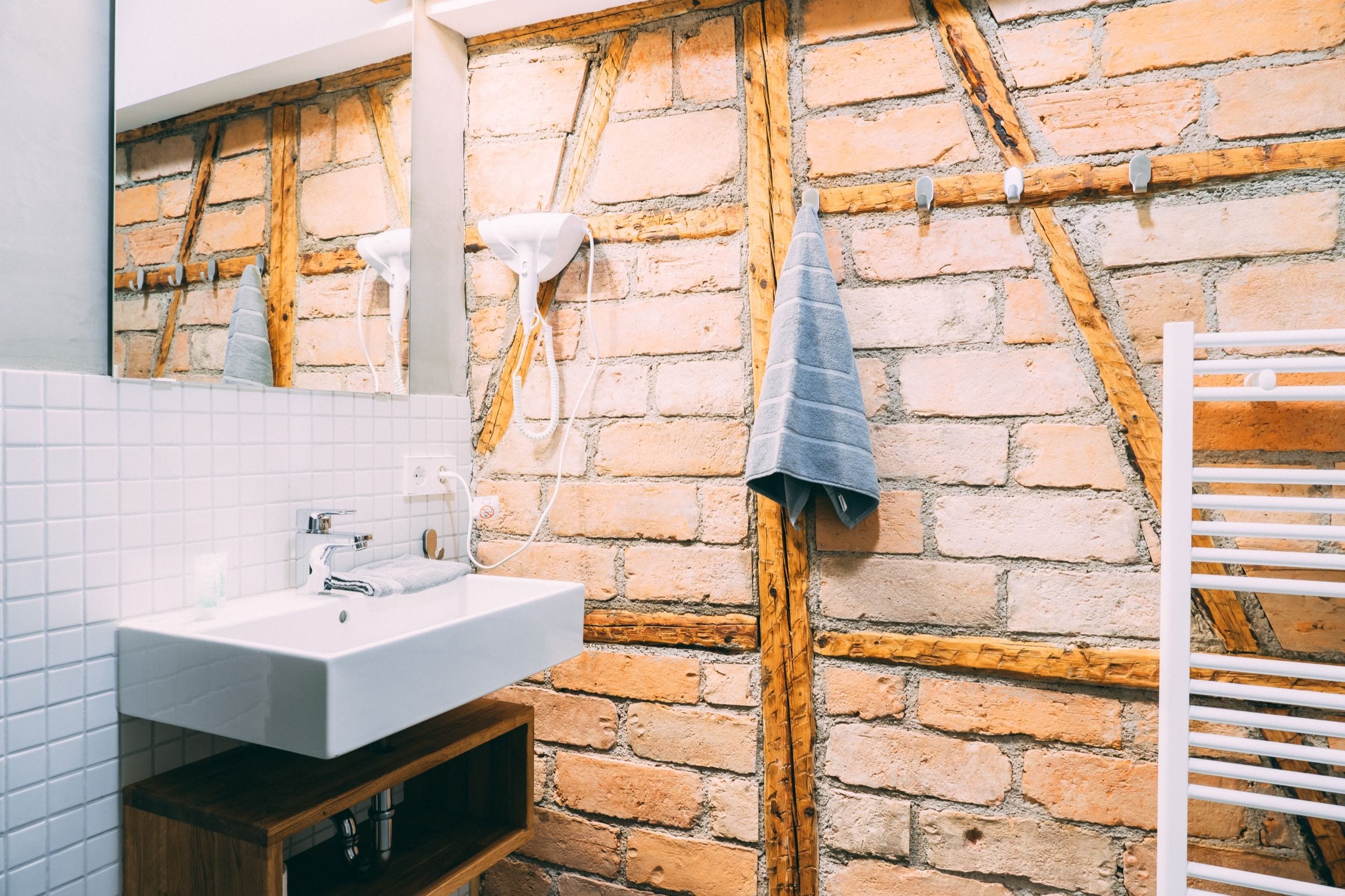 Un baño con un lavabo blanco, un espejo y una pared de ladrillo.