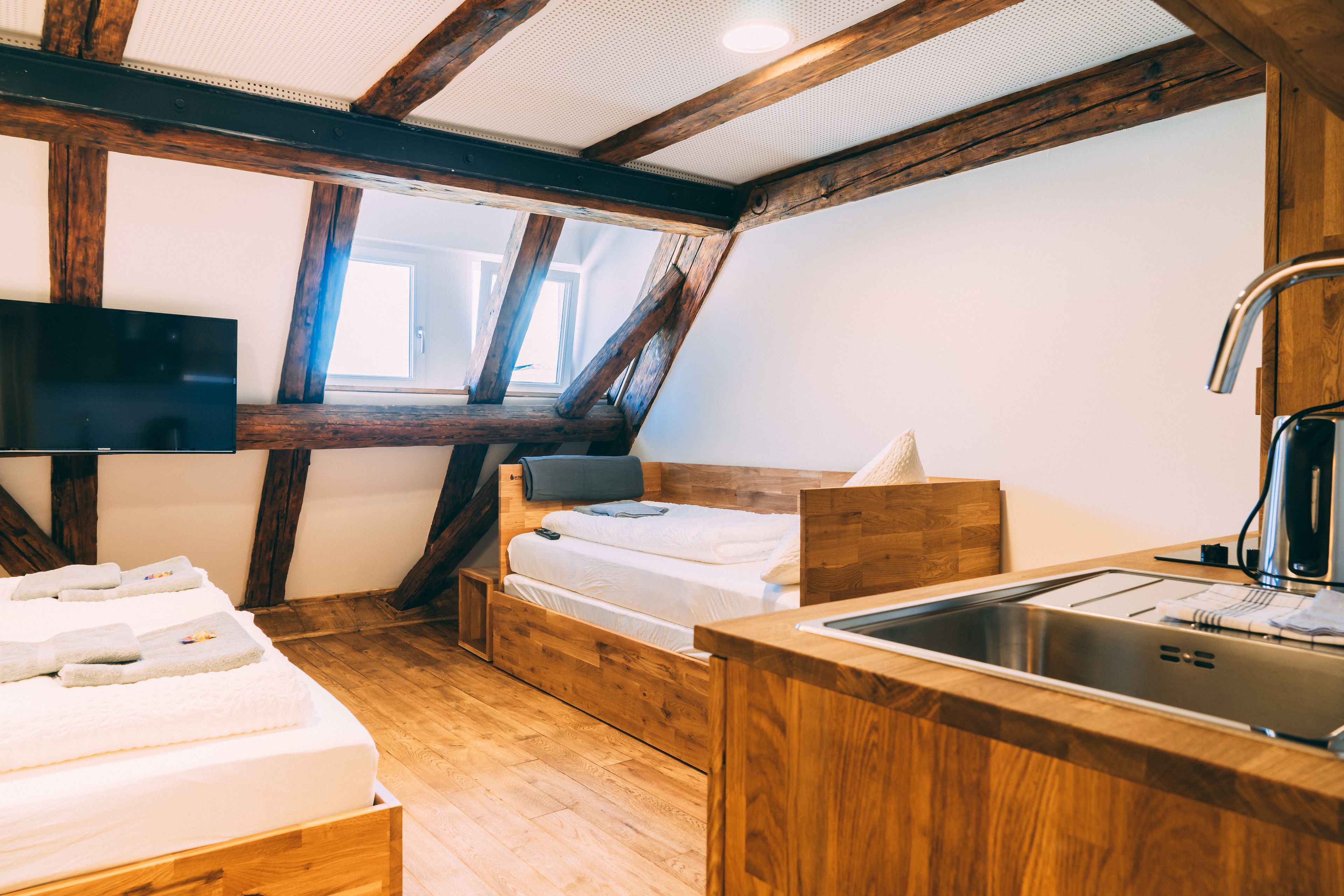 A compact room with a bed, a small desk, a sink, and a television.