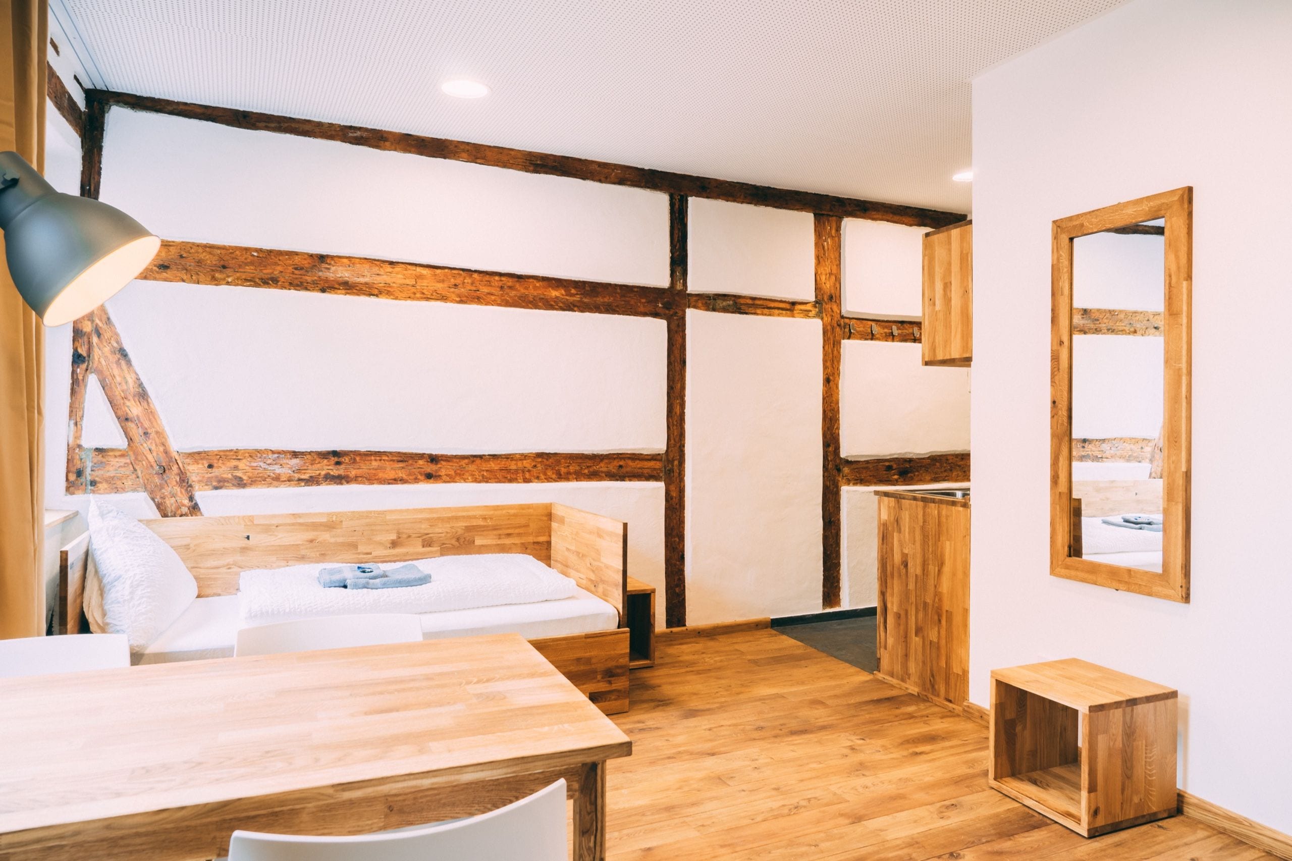 Une pièce avec un plafond en bois, un lit avec une literie blanche, une table en bois et une petite armoire en bois.