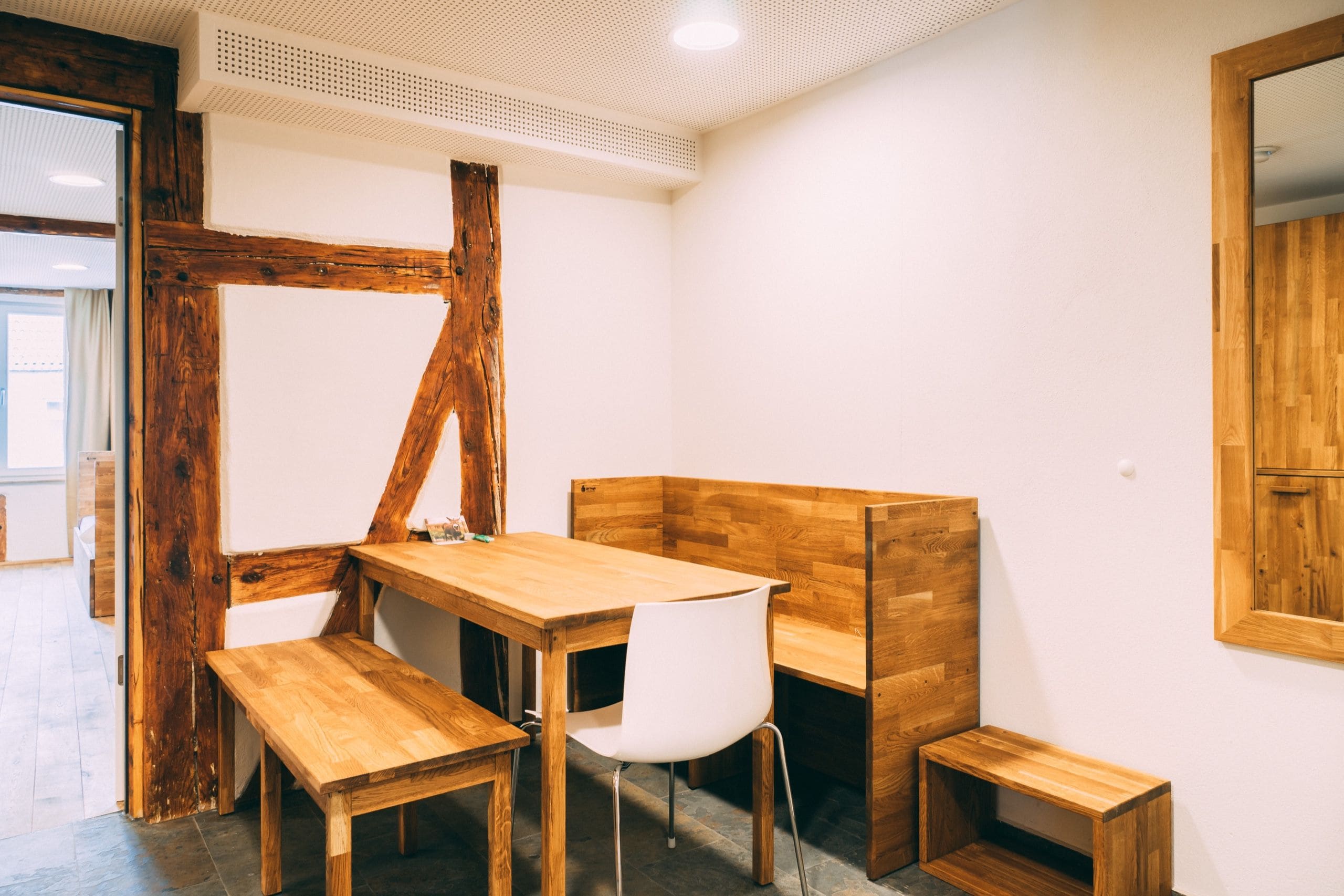 Une pièce avec une table et des bancs en bois, une chaise blanche et un meuble en bois.
