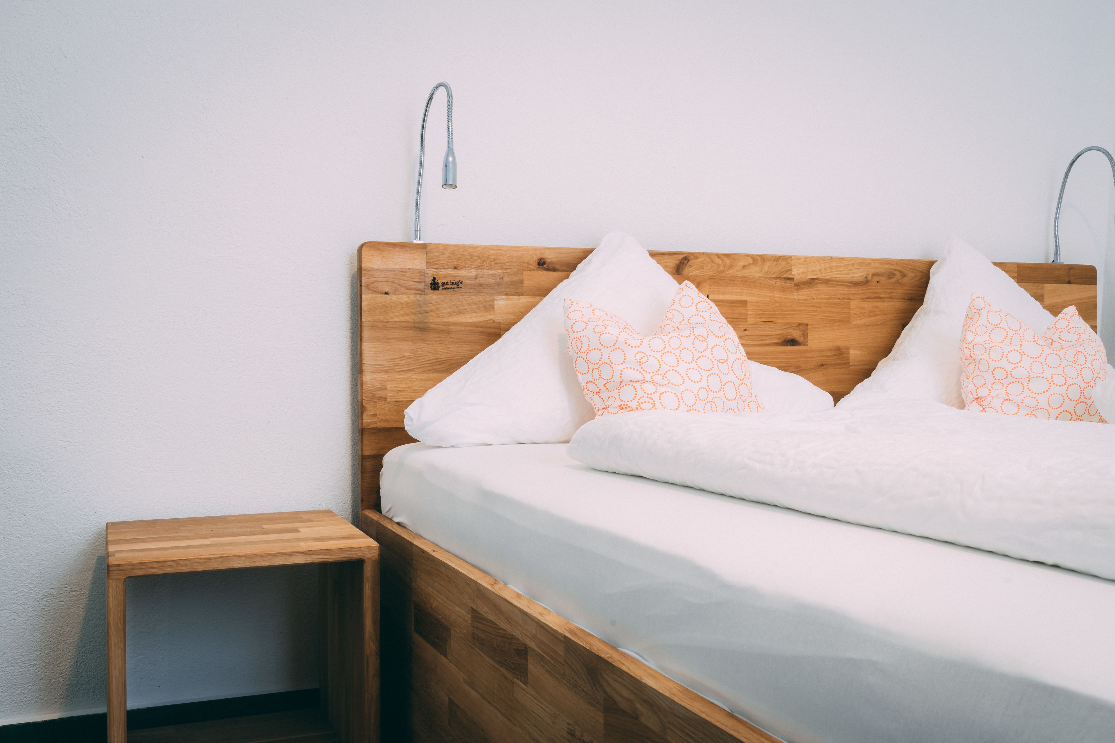 Un letto singolo con testiera in legno, biancheria da letto bianca e due cuscini decorati.