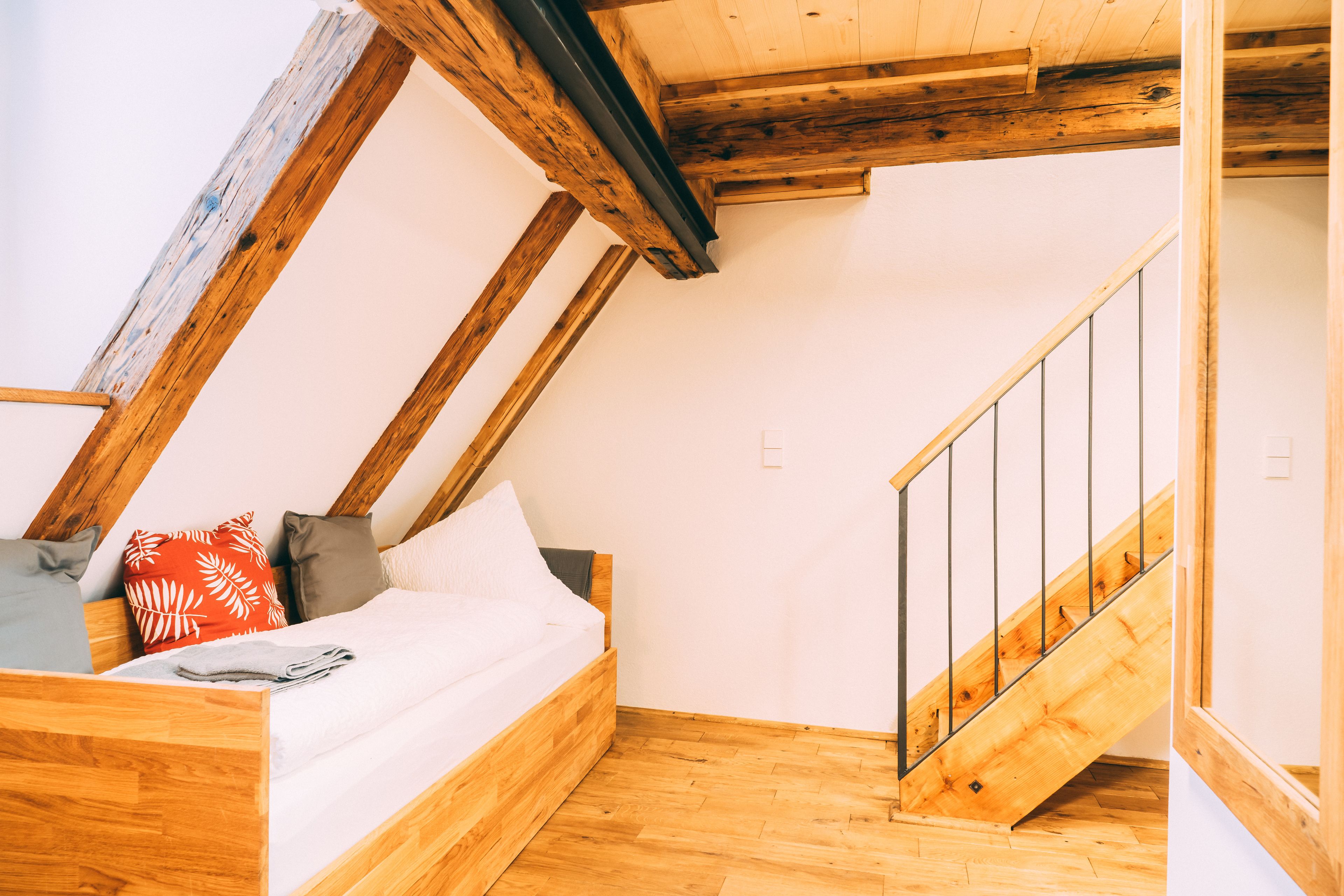 A loft bedroom with a wooden bed, a staircase, and exposed wooden beams.