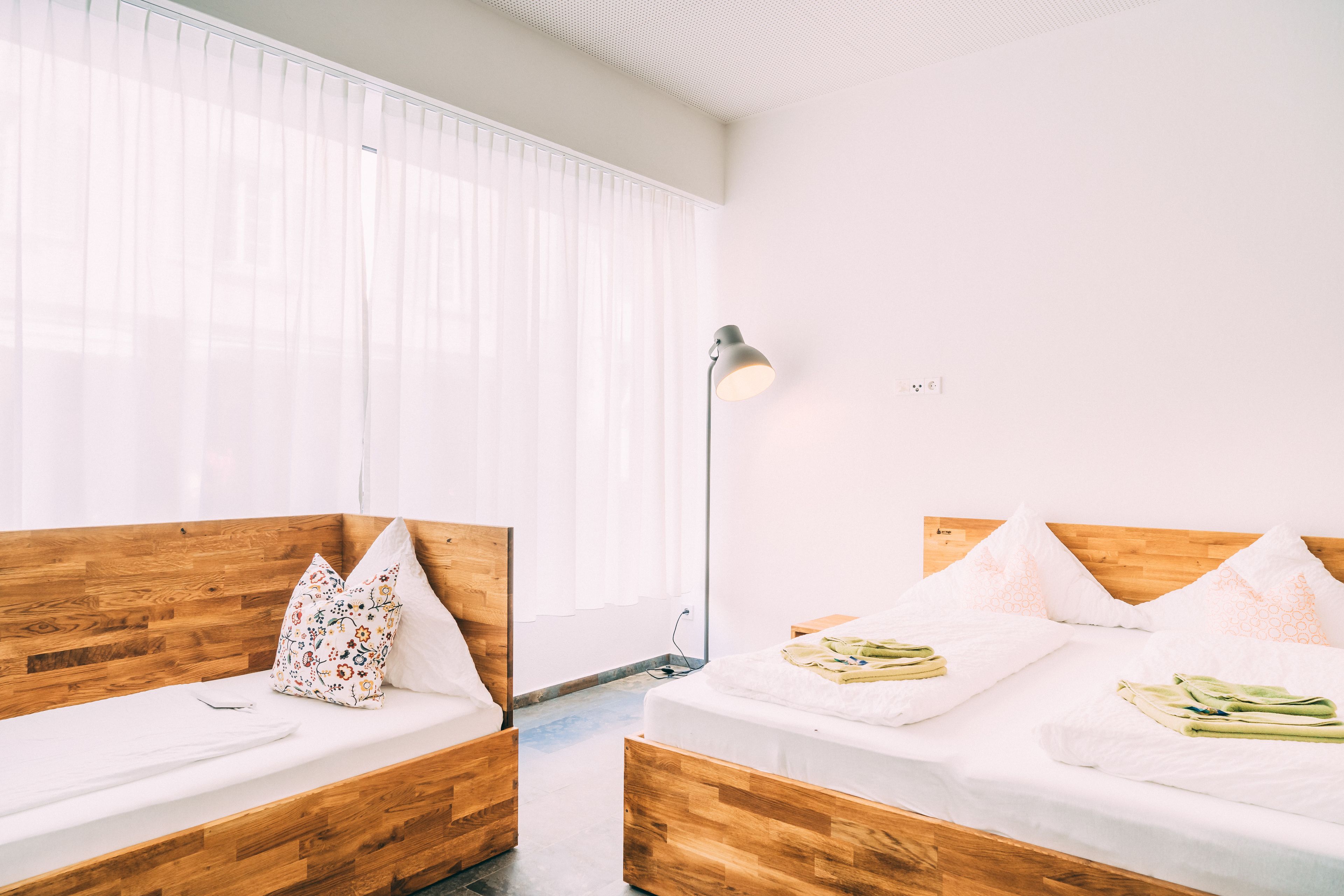 Quarto de hotel moderno com duas camas de madeira, roupa de cama branca e um abajur.
