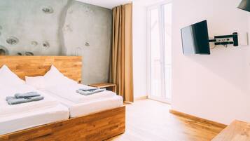 Una habitación de hotel moderna con una cama de madera, un televisor de pantalla plana en la pared y un ventanal con cortinas.