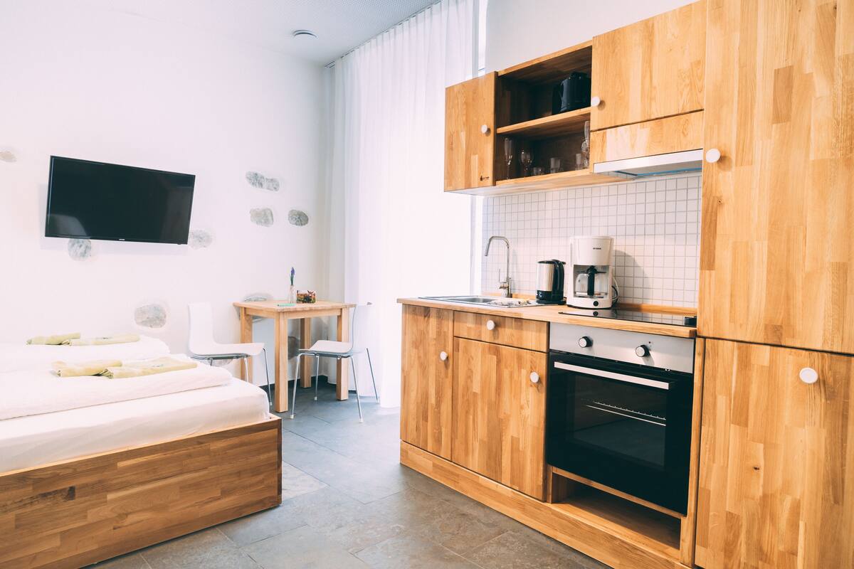 A compact hotel room with a bed, a small kitchenette, a TV, and a dining area.