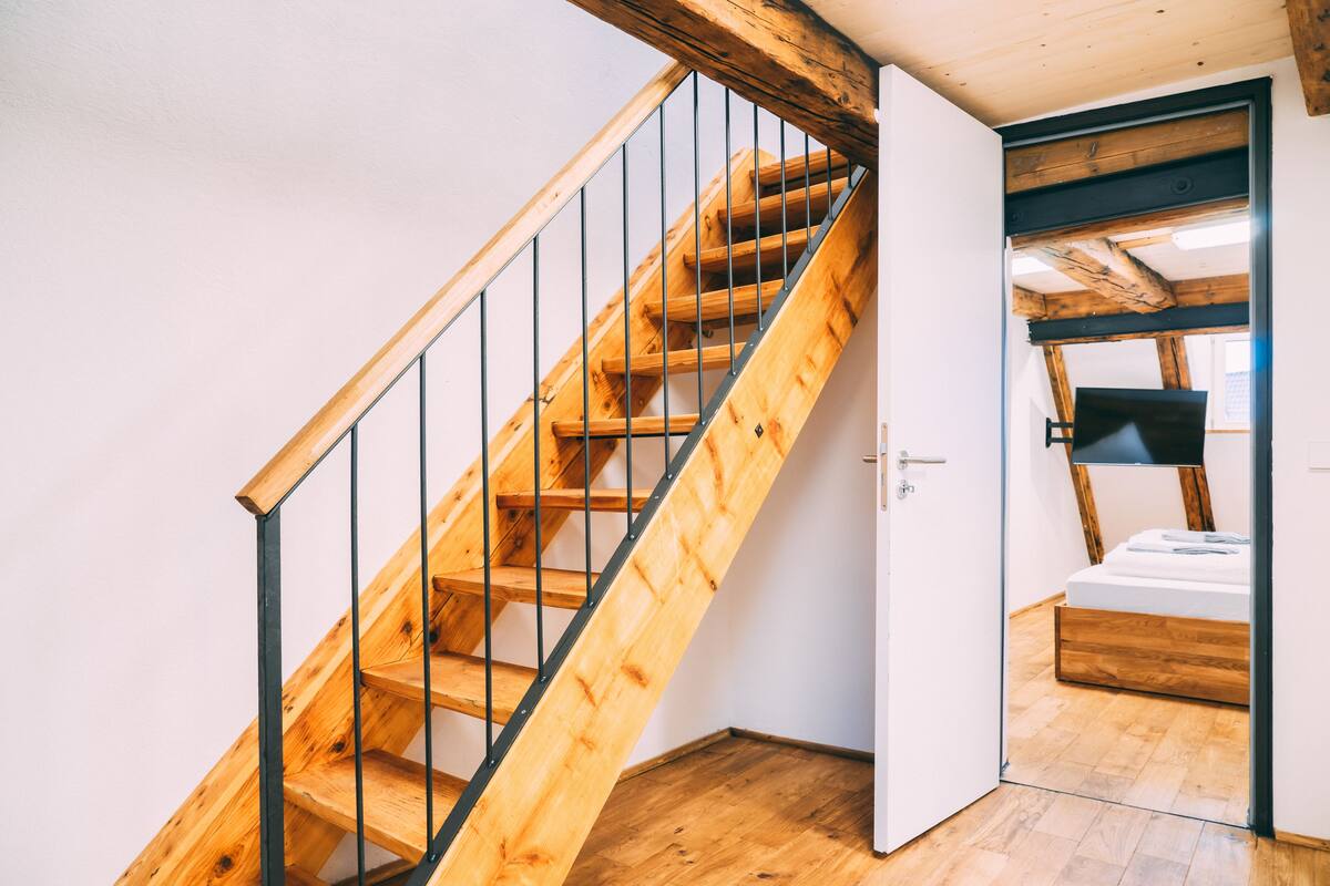 A wooden staircase with metal railings leading to a bedroom with a wooden bed frame and a window.
