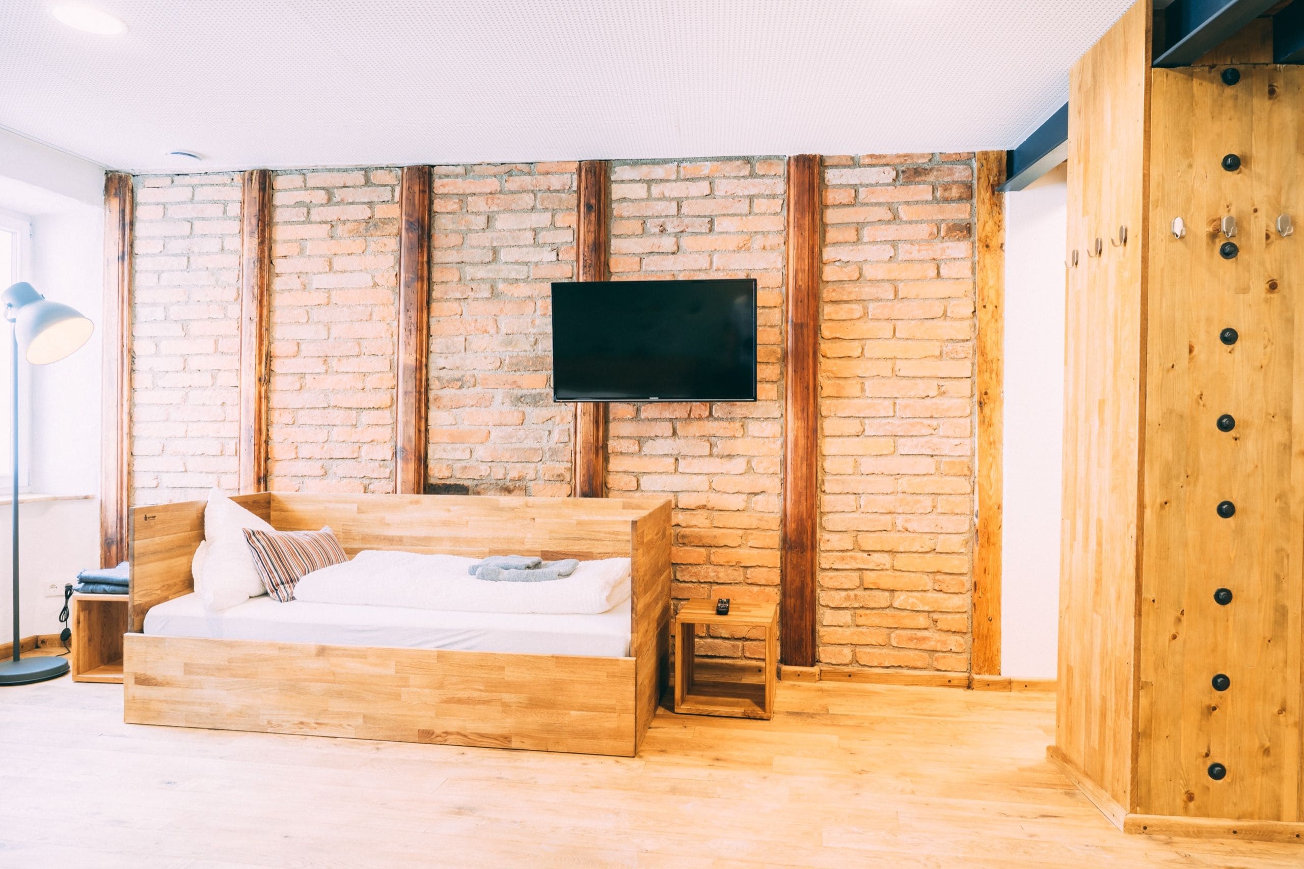 A room with a wooden bed, a brick wall, a mounted TV, and a wooden cabinet.